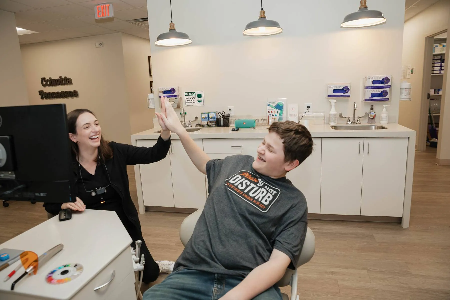Smiling orthodontic assistant giving a high-five to a young patient in a modern clinic setting, emphasizing a friendly and welcoming atmosphere at Lucas Orthodontic Group in Columbia, Tennessee.